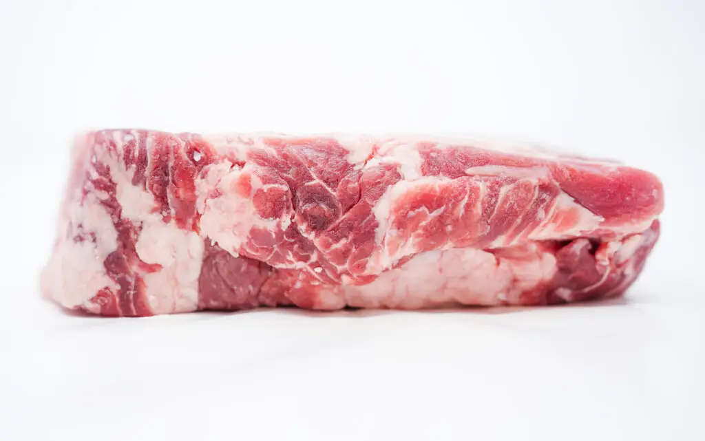 A close-up image of a thick, raw ribeye steak displaying rich, intricate marbling throughout its tender flesh, showcasing its quality and freshness on a simple, clean background.