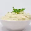 A bowl of rich elephant garlic mashed potatoes, topped with a melting pat of butter and sprinkled with fresh chives, highlighting its creamy texture and subtle garlic taste.
