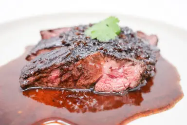 A succulent seared hanger steak rests on a plate, glazed with a rich balsamic shallot reduction that accentuates its deep, caramelized crust, showcasing the dish's enticing aroma and gourmet presentation.