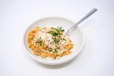 A bowl of pork belly carbonara, featuring creamy pasta entwined with chunks of crispy pork belly, garnished with grated Parmesan and fresh herbs, embodying a rich and indulgent fusion of flavors.