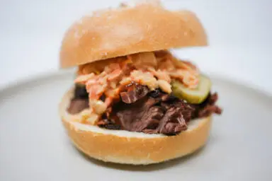 A delectable sweet and tangy brisket sandwich on ciabatta bread, layered with juicy beef and vibrant kimchi coleslaw, creating a colorful and appetizing meal.