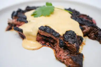 A succulent sirloin steak with a dark, rich crust from a coffee-ancho chili rub, drizzled with a smooth, spicy pepper jack cheese sauce, garnished with fresh parsley on a white plate.