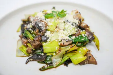 A vibrant Grilled Leeks and Portobello Mushroom Salad, showcasing charred leeks and mushrooms atop a bed of greens, drizzled with dressing, and sprinkled with Parmesan and parsley.