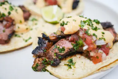 Plated Coffee-Ancho Sirloin Steak Tacos drizzled with creamy Pepper Jack Sauce, nestled in soft tortillas and topped with vibrant, fresh tomato salsa and a sprinkle of cilantro, embodying a perfect blend of smoky, spicy, and tangy flavors.