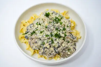 A creamy Wild Mushroom Stroganoff served in a white bowl, richly garnished with fresh chopped parsley, showcasing a variety of wild mushrooms in a thick, savory sauce.