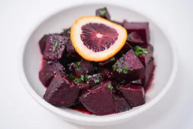 A vibrant dish of Blood Orange Ginger Glazed Roasted Beets, showing cubed beets coated in a glossy, reddish-orange glaze, sprinkled with fresh green parsley for a colorful contrast.