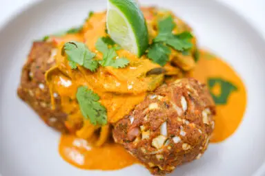 A warm, inviting dish of Coconut Curry Chicken Meatballs, featuring golden-brown meatballs nestled in a rich, creamy coconut curry sauce, garnished with fresh cilantro and a lime wedge.