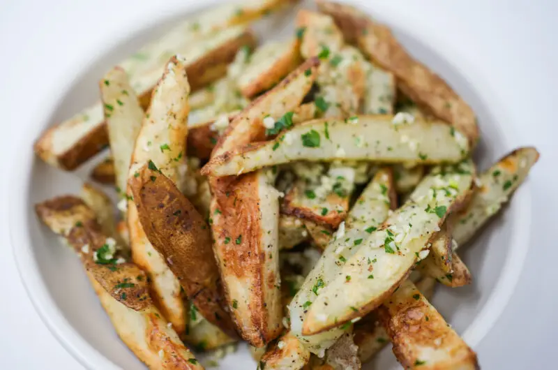 A bowl of golden-brown Garlic Parsley Steak Fries, sprinkled with fresh chopped parsley and minced garlic, showcasing their crispy exteriors and fluffy interiors.