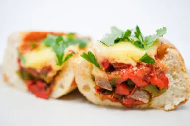 A toasted hoagie roll overflowing with slices of grilled Italian sausage, charred red and green bell peppers, and poblano, all topped with a rich homemade marinara sauce and melted Monterey Jack cheese, creating a colorful and appetizing meal.
