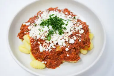 Mediterranean-Inspired Ground Lamb Ragu served over gnocchi pasta, topped with crumbled goat cheese and fresh parsley.