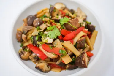 A colorful Sesame Soy Shiitake Mushroom Salad featuring quartered shiitake mushrooms, slices of red bell pepper, bamboo shoots, and onion, all tossed with a glossy, cilantro-infused sesame soy dressing.