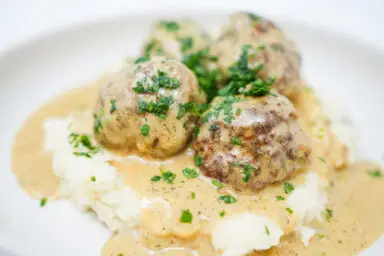 A plate of Creamy Dill Swedish Meatballs served over fluffy mashed potatoes, topped with a rich, herb-infused cream sauce and garnished with fresh parsley.