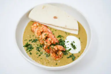 A vibrant image of Spicy Tomatillo Shrimp Bowls, showcasing juicy broiled shrimp on a bright green tomatillo sauce, garnished with fresh cilantro and a dollop of sour cream, accompanied by a side of warm tortillas.